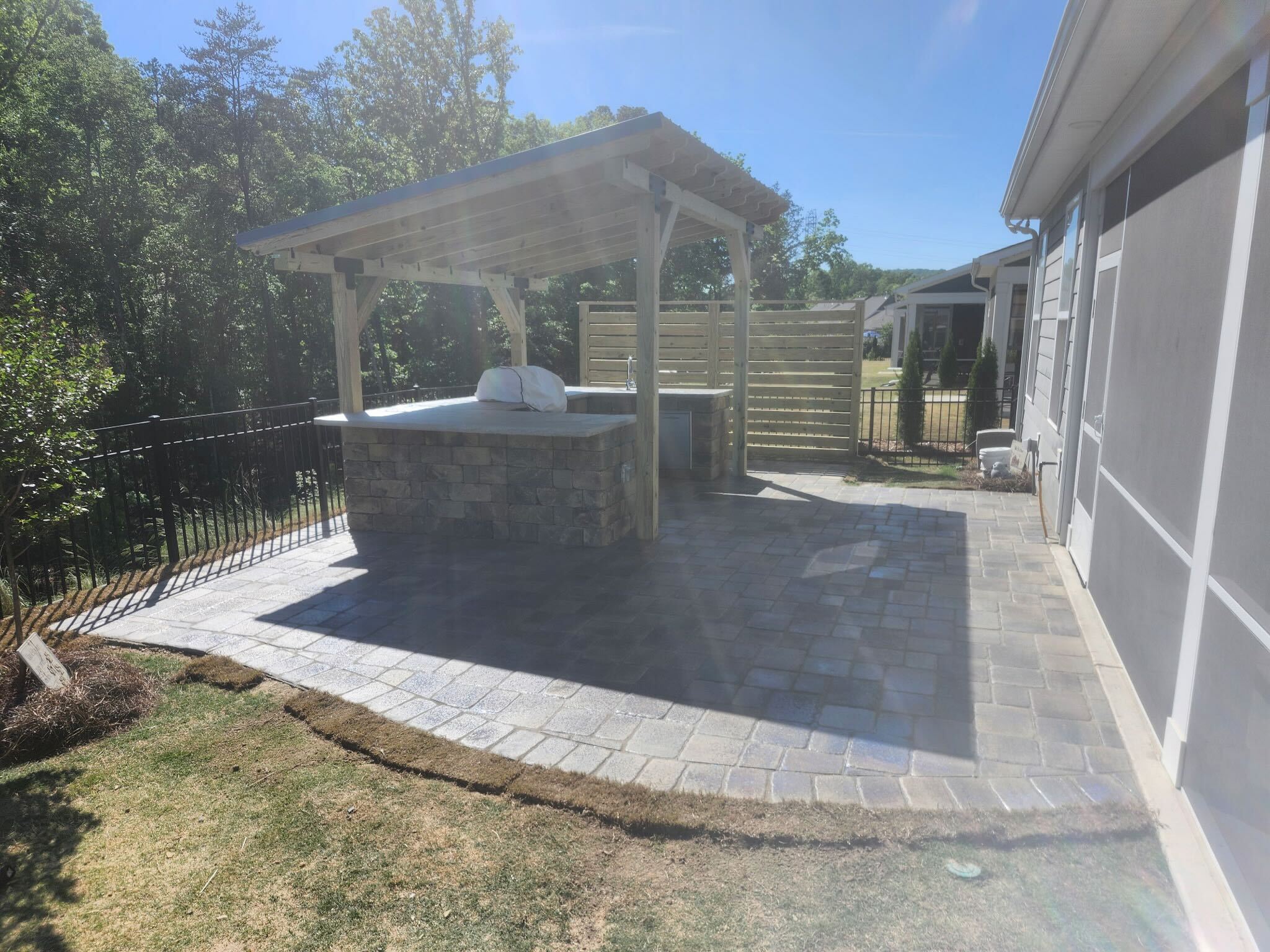 Paver patio with stone outdoor kitchen under a cedar pergola